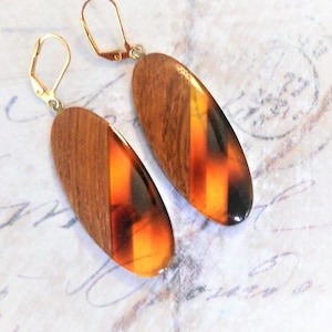 Puede incluir: Un par de pendientes colgantes ovalados con cierres de palanca dorados. Cada pendiente combina una sección de madera con una sección con estampado de carey en tonos marrón, ámbar y negro. Un accesorio elegante.