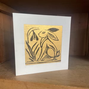 Handgesneden en gedrukte lino-wenskaart met origineel ontwerp van een haas op achterpoten, paaskaart. Zwarte inkt op goud, art-deco-gevoel