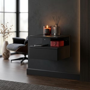 May include: A matte black floating wall-mounted bedside table featuring a single storage drawer and an open shelf. The top surface holds a lit candle in a glass jar and a reed diffuser, while the shelf contains a smartphone and a red jewellery box.