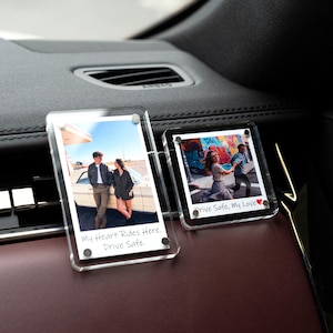Op de afbeelding: Twee heldere acryl foto auto-accessoires, elk met een foto. Eén foto toont een stel bij een auto, met de tekst "My Heart Rides Here. Drive Safe." De andere toont een stel met de tekst "Drive Safe, My Love".