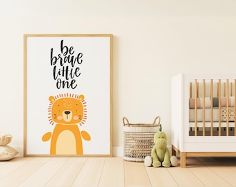 May include: A framed print with a white background and black text that reads "Be brave little one". A cartoon lion with orange fur and a yellow belly is in the center of the print.