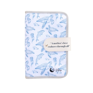May include: White and blue baby changing pad with a sea life pattern featuring turtles, dolphins, and jellyfish. The pad has a gray border and a beige strap with the text "A mother's love endures through all".
