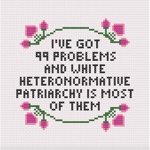 May include: Cross-stitch design on white fabric. The text reads "I'VE GOT 99 PROBLEMS AND WHITE HETERONORMATIVE PATRIARCHY IS MOST OF THEM" in black. Pink floral accents with green stems and leaves frame the text.