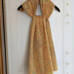 Può includere: Una sciarpa gialla con motivo paisley appesa a un appendiabiti. La sciarpa è realizzata in un tessuto morbido e leggero e ha un drappeggio fluido.