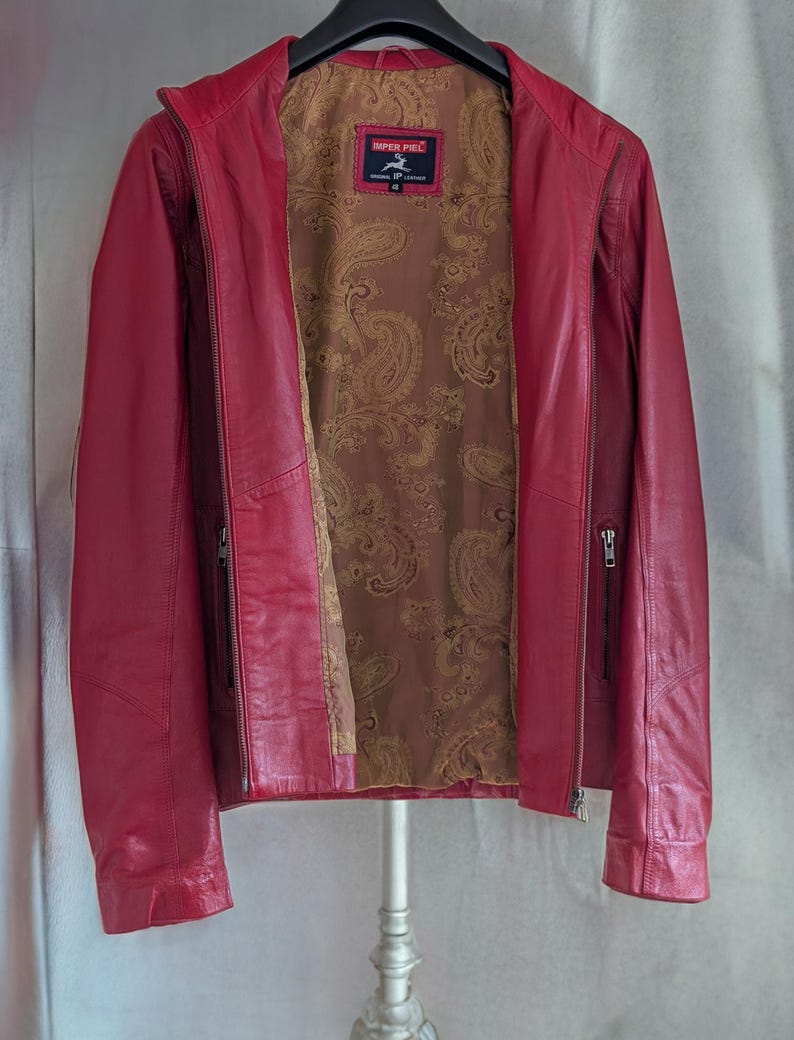 Op de afbeelding: Een rood leren jack met een paisley voering. Het jack heeft een ritssluiting en twee zakken aan de voorkant. Het label op het jack luidt "Imper Piel" en "Echt leer".