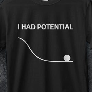 Könnte beinhalten: Schwarzes T-Shirt mit dem Text "I HAD POTENTIAL" über einer weißen Grafik eines Balls, der eine gekrümmte Bahn hinunterrollt. Das Shirt hat einen Rundhalsausschnitt und kurze Ärmel. Das Bild enthält auch Werbetext und Logos.