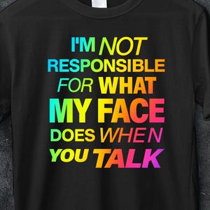 Può includere: T-shirt nero con la scritta "I'M NOT RESPONSIBLE FOR WHAT MY FACE DOES WHEN YOU TALK" in colori arcobaleno. La maglietta è appesa a una gruccia bianca. Un adesivo rosso dice "50% OFF" e "MINIMUM BUY 5".