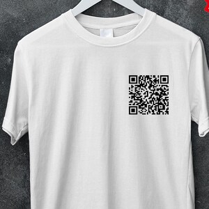 Può includere: Una maglietta bianca con un codice QR nero stampato sul petto. La maglietta è appesa a una gruccia bianca su uno sfondo grigio scuro. Un cerchio rosso con la scritta "50% OFF MINIMUM BUY 5 CODE: BULK50" si trova in alto a destra.