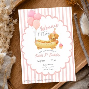 May include: A birthday invitation card featuring a dachshund dressed as a hot dog, wearing a party hat, with three pink balloons and a cupcake. The text reads Weenie Bit Older, join us to celebrate Juliet's 5th Birthday, August, 12pm, Party Venue, 123 Party Lane, Party Town, RSVP by 25/07 Michelle 0434 456 345.