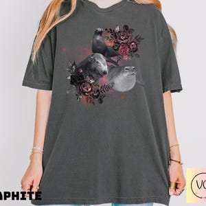 May include: Graphite-colored t-shirt featuring a graphic of three seals surrounded by dark red and black roses. The seals are in shades of gray and white. The word "GRAPHITE" is printed in black at the bottom of the shirt.