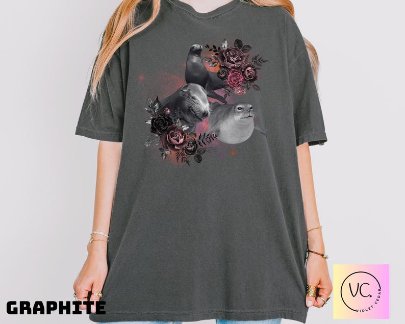 May include: Graphite-colored t-shirt featuring a graphic of three seals surrounded by dark red and black roses. The seals are in shades of gray and white. The word "GRAPHITE" is printed in black at the bottom of the shirt.