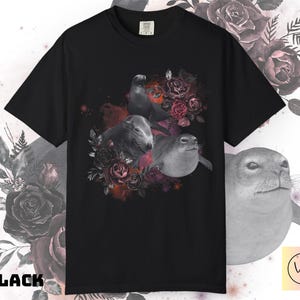 May include: Black t-shirt featuring a graphic of three seals surrounded by dark red and pink roses. The seals are in grayscale, contrasting with the vibrant floral arrangement. The word "BLACK" is printed in bold white letters.