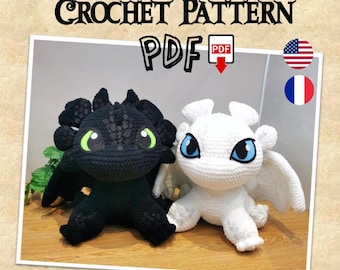May include: Crochet pattern PDF for making two plush dragons, one black and one white. The dragons have large eyes and are sitting on a wooden surface. The pattern is available in English and French.
