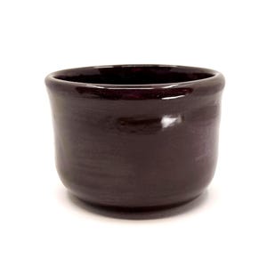 以下が含まれることがあります： 光沢のある仕上げの、小さな濃い茶色のセラミックボウル。ボウルは丸みを帯びた底とわずかにフレアしたリムを持っています。内側は深く、豊かな茶色です。ボウルはおそらく手作りで、少量のサービングに適しています。