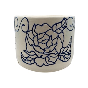 Puede incluir: Maceta de cerámica blanquecina con un diseño de rosa azul marino dibujado a mano. El patrón floral envuelve el cuerpo cilíndrico de la maceta. Remolinos decorativos pintados cerca del borde. Una pieza única para la decoración del hogar.