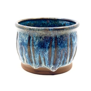 May include: A handcrafted ceramic planter with a round shape and a textured, glazed surface. The planter features a blend of blue and brown hues, with a dark brown base. The interior is dark blue, and the rim is a darker shade of blue.