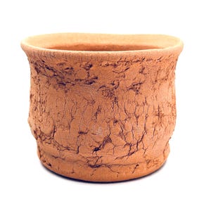 Pode incluir: Um pequeno vaso redondo de cor terracota com uma superfície texturizada e rachada. A borda é um tom de castanho mais claro. O vaso é projetado para uso interno ou externo e é adequado para plantas pequenas.