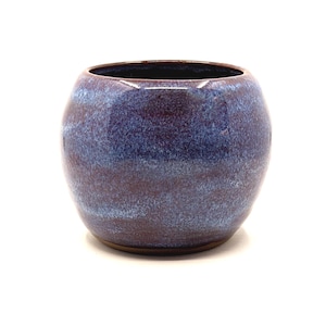 May include: A round, ceramic vase with a dark blue and maroon glaze. The vase has a wide opening and a smooth, glossy finish. The color transitions from dark maroon at the base to a deep blue at the top.