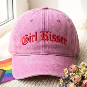 Peut inclure: Une casquette de baseball rose avec une finition en tissu délavé, ornée du texte Girl Kisser brodé en lettres gothiques rouges sur le panneau avant. La casquette présente une calotte structurée, une visière incurvée et des œillets cousus.