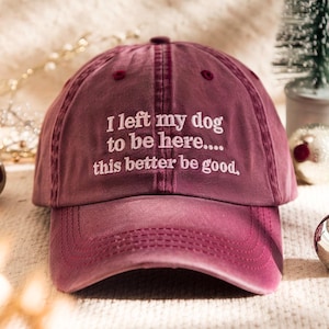 May include: A maroon baseball cap with the embroidered text, "I left my dog to be here.... this better be good." The cap has a curved brim and a six-panel design. The hat is made of a soft, washed cotton material.