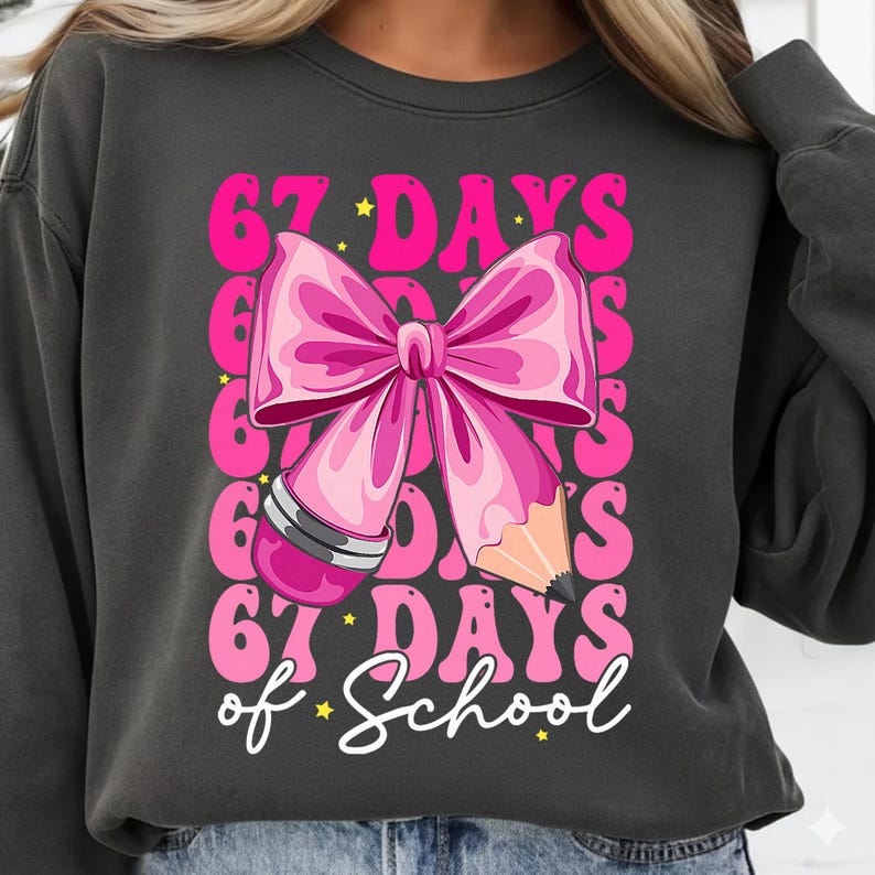 May include: Dark grey sweatshirt featuring a pink bow and pencil graphic. The design includes the text "67 DAYS of School" in pink and white, with star accents. A fun and colourful design for back-to-school.