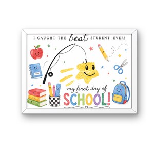 Op de afbeelding: Een ingelijste print met de tekst I CAUGHT THE best STUDENT EVER! en my first day of SCHOOL! met kleurrijke illustraties van een lachende appel, notitieboek, hengel, ster, potlood, schaar, rugzak en boeken in een pennenhouder.