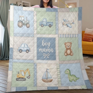 Puede incluir: Una manta acolchada para bebé con un diseño de patchwork que presenta varios vehículos, un oso de peluche y un dinosaurio. El cuadrado central dice "boy mama". La paleta de colores incluye azul, verde y beige.