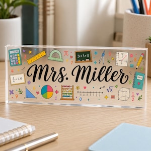 May include: A rectangular clear acrylic desk sign featuring the name Mrs. Miller in black script. The surface is decorated with colorful math-themed graphics including a calculator, ruler, protractor, abacus, compass, and various geometric shapes.