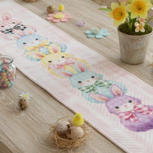 May include: A pastel pink Easter table runner featuring a repeating pattern of watercolor bunny rabbits with colorful bowties. The runner is decorated with a chevron pattern and is surrounded by Easter-themed decorations, including eggs and flowers.