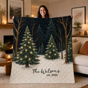 Könnte beinhalten: Eine gesteppte Wohndecke mit einer winterlichen Waldszene, schneebedecktem Boden, dunklen Bäumen und beleuchteten Weihnachtsbäumen. Der Text "The Wilsons" und "est. 2026" ist in schwarzer Schreibschrift und Serifenschrift unten auf der Decke gedruckt.