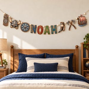 Puede incluir: Un estandarte decorativo de pared con el nombre NOAH en letras texturizadas de colores, intercaladas con adornos de temática vikinga que incluyen un casco, un escudo, un cuerno, hachas cruzadas y un barco, en un cordón de cuentas blancas.