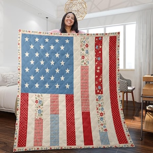 Op de afbeelding: Een doorgestikte plaid met een patchworkontwerp van de Amerikaanse vlag. Het blauwe kanton bevat witte sterren, terwijl de strepen bestaan uit afwisselende verticale panelen met rode, witte en blauwe bloemen-, ruitjes- en stippenpatronen.