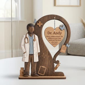 May include: A wooden doctor figurine with a white coat and stethoscope stands next to a wooden frame. The frame has a heart-shaped plaque with the name "Dr. Andy" and a message. Decorative butterflies and medical symbols are also present.