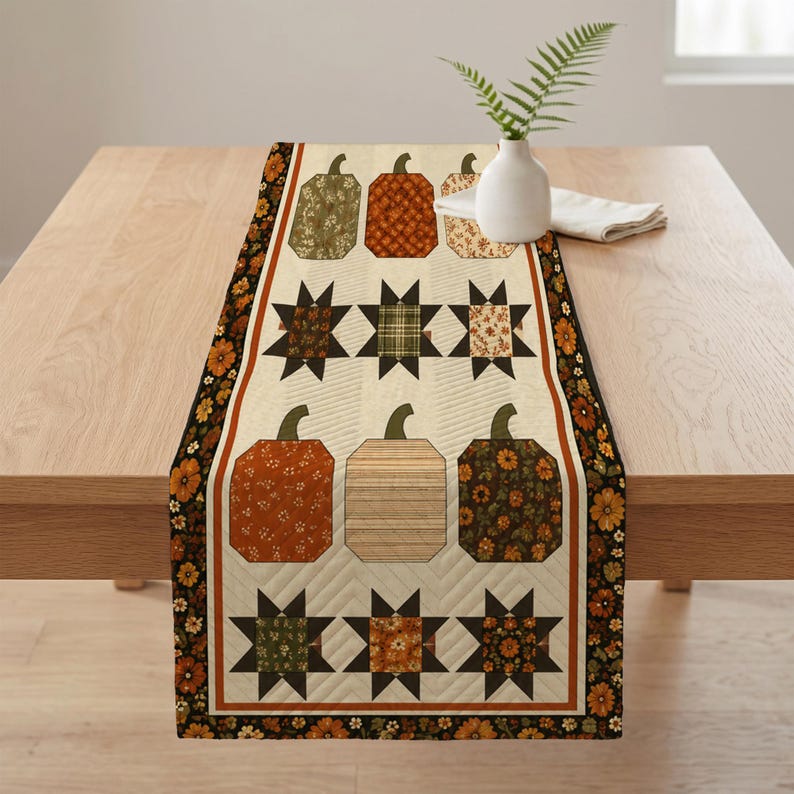 May include: A rectangular quilted table runner featuring a cream-colored background with a repeating pattern of pumpkins and star shapes in shades of orange, brown, green, and tan. The runner has a dark border with a floral print.