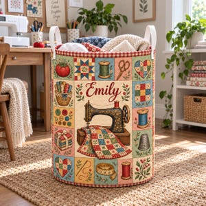 May include: A cylindrical fabric storage basket featuring a quilted patchwork design with sewing-themed illustrations including a sewing machine, spools of thread, scissors, buttons, and a thimble. The name Emily is printed in red script in the center.