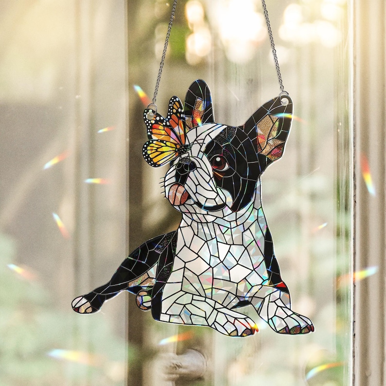 Peut inclure: Un attrape-soleil en vitrail en forme de bouledogue fran&ccedil;ais avec des segments noirs et blancs. Un papillon monarque aux ailes orange, noires et blanches repose sur une oreille. L'objet est suspendu par une cha&icirc;ne argent&eacute;e et inclut du verre iris&eacute;.
