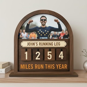 Könnte beinhalten: Holz-Laufprotokoll mit einem Foto eines Mannes, der einen Rennsieg feiert. Das Protokoll zeigt "JOHN'S RUNNING LOG" und "MILES RUN THIS YEAR" mit der Zahl 1254. Der Rahmen ist dunkelbraun.