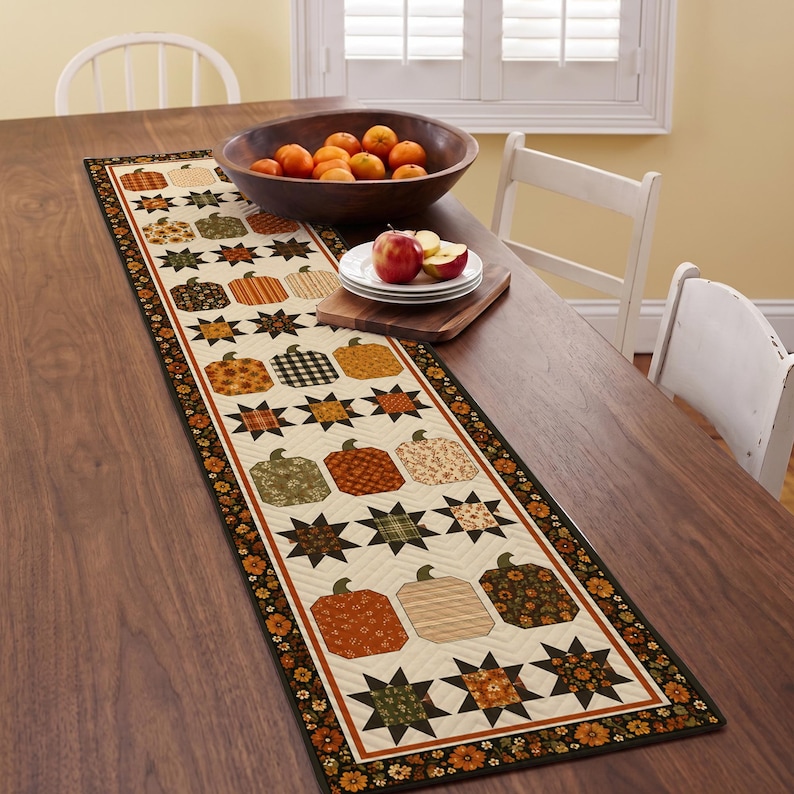 May include: A rectangular quilted table runner featuring a repeating pattern of fabric pumpkins and eight-pointed stars in shades of orange, brown, green, and cream. The runner has a dark floral border and is stitched with a chevron quilting design.