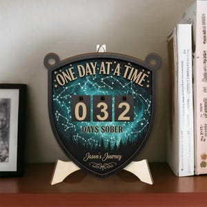 May include: A wooden desk calendar with the text "ONE DAY AT A TIME" and "DAYS SOBER". The calendar displays "032" days sober. The background features a starry night sky and a forest silhouette. The calendar is personalized with the name "Jason's Journey".
