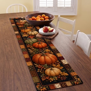 May include: A rectangular table runner featuring a black center panel decorated with a pattern of orange and green pumpkins, autumn leaves, and berries, bordered by a patchwork design of squares in shades of brown, orange, and yellow.