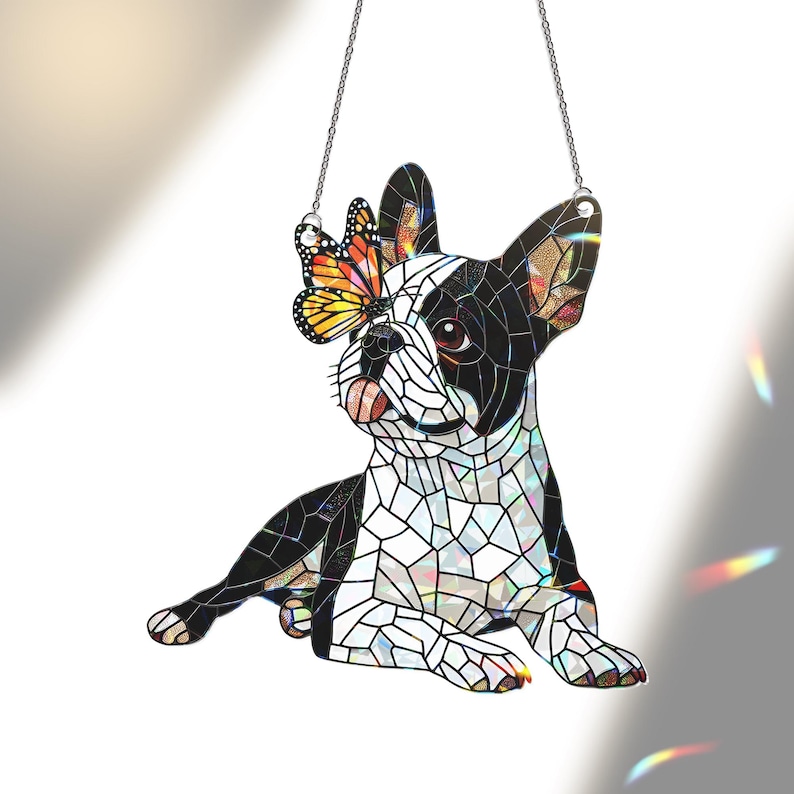Peut inclure: Un attrape-soleil en vitrail en forme de bouledogue fran&ccedil;ais compos&eacute; de segments noirs et blancs. Un papillon monarque orange et noir vif repose sur une oreille. L'objet est suspendu par une fine cha&icirc;ne en m&eacute;tal argent&eacute; pour la fen&ecirc;tre.