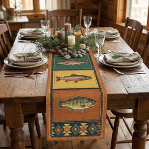 May include: A rustic dining table set for a meal, featuring a colorful table runner with fish illustrations. The runner has a green, yellow, and orange background with fish designs. Candles, pinecones, and river rocks decorate the table.