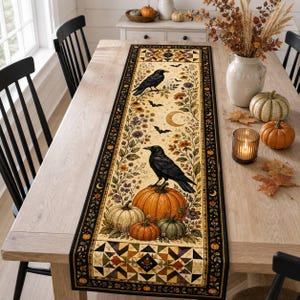 May include: A rectangular table runner featuring a cream-coloured centre panel with black crows, orange pumpkins, autumn flowers, bats, and a crescent moon. The runner has a wide black border with a geometric quilt-style pattern at both ends.