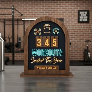 Könnte beinhalten: Gym-Log aus Holz mit dunklem Hintergrund und Neontext, der "345 Workouts Crushed This Year" lautet. Das Logbuch zeigt Symbole für Gewichte und eine Kettlebell. Auf der Unterseite des Logbuchs steht "William's Gym Log".