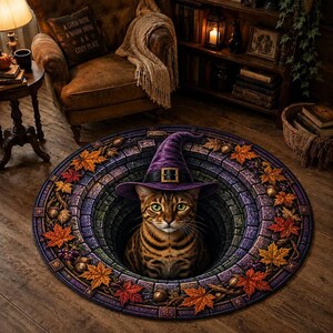 Peut inclure: Un tapis rond présentant une illusion d'optique 3D d'un puits en pierre. Un chat tigré brun portant un chapeau de sorcière violet avec une boucle dorée est assis dans le puits. La bordure est ornée de feuilles d'automne, de glands et de raisins.