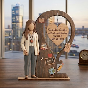 May include: A wooden teacher figurine with a heart-shaped plaque that reads "She speaks with wisdom and teaches with kindness." The figurine includes a teacher figure, books, an apple, a globe, and a pencil. The teacher is wearing a cream-colored cardigan and gray pants.