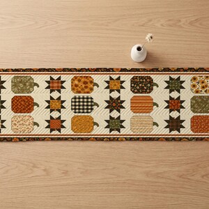 May include: A rectangular quilted table runner featuring a repeating pattern of fabric pumpkins and eight-pointed stars in shades of orange, brown, green, and cream. The runner has a dark floral border and a cream-colored background with chevron stitching.