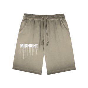 May include: Khaki-coloured shorts with a drawstring waist and pockets. The shorts feature the word "MIDNIGHT" in white, with dripping lines beneath. The fabric has a faded, ombre effect, transitioning from a darker shade at the top to a lighter tone at the bottom.