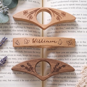 May include: Three wooden hair accessories with engraved designs. The top piece is light wood with floral engravings and a centre hole. The middle piece is light wood with butterflies and the name William. The bottom piece is dark wood with leaf engravings and a centre hole.