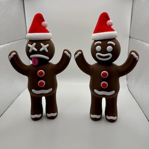 May include: Two gingerbread men figurines, one with a happy face and the other with a deadpan expression and a tongue sticking out. Both are wearing red Santa hats and have white icing details.